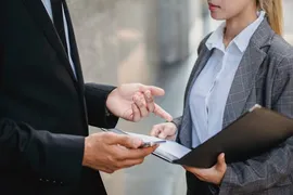 Two people in suits talking over a folder.