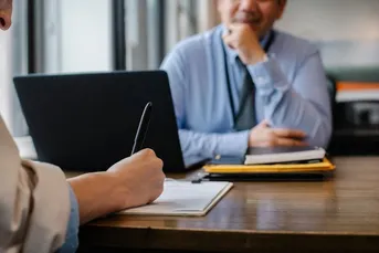 A man sitting across from a person writing.