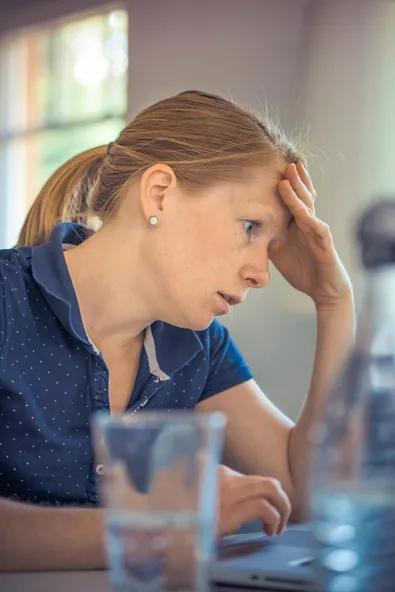 Stressed out woman looking at computer with her hand on her forehead.