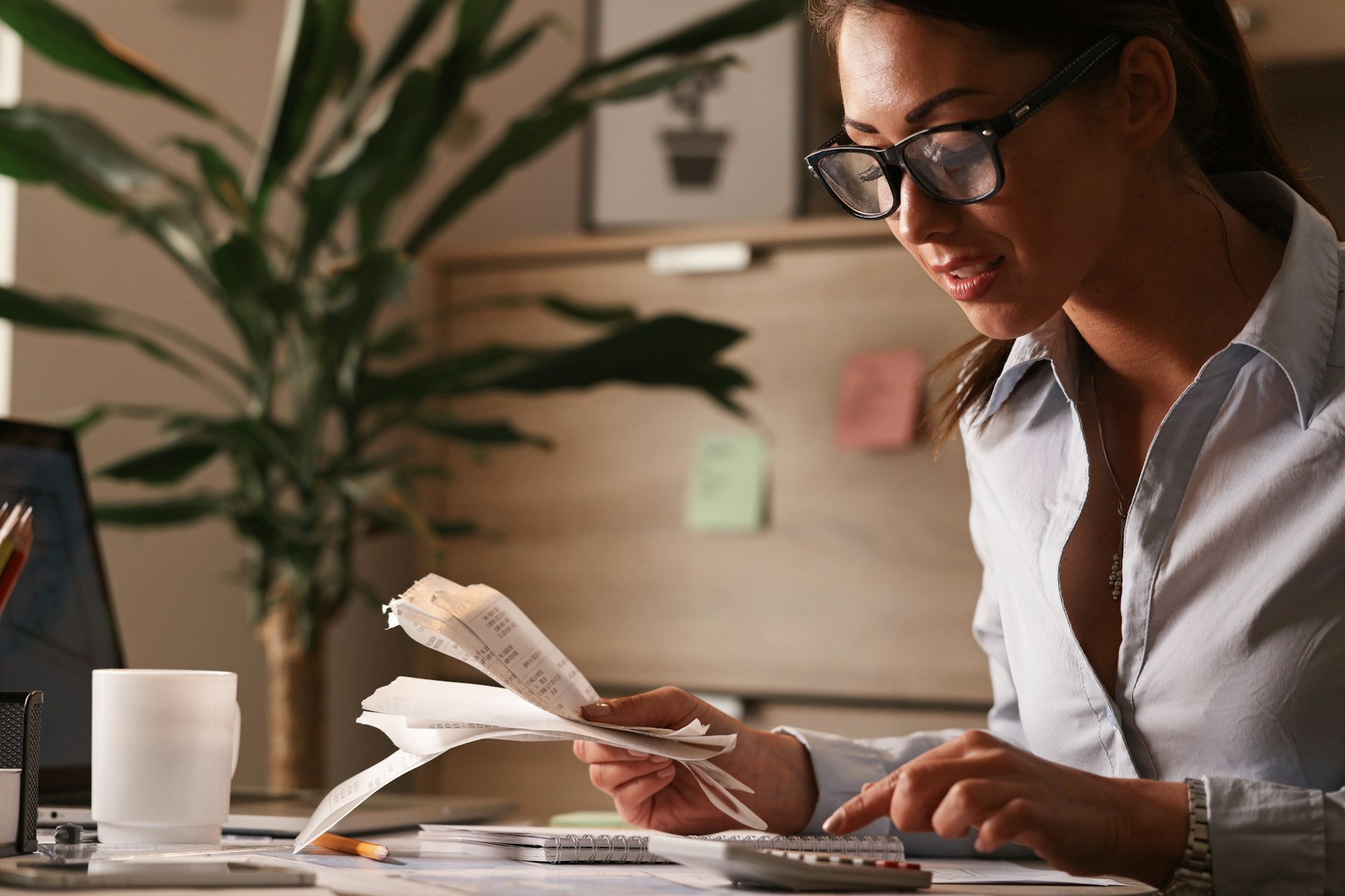 Woman holding receipts and typing on a calculator.